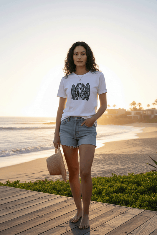 Model standing on a wooden deck by the beach at sunset, wearing a graphic tee by Studio Viekay and denim shorts.