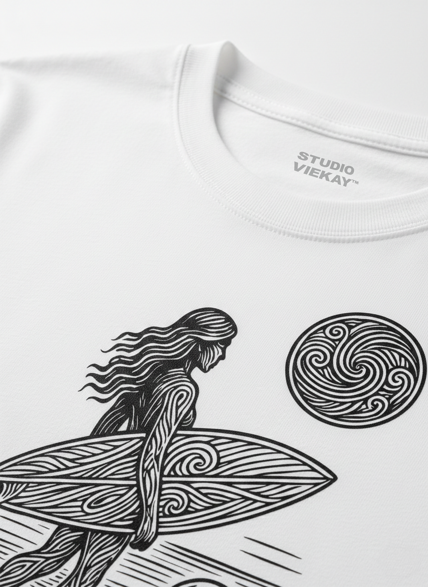Close-up of a white Studio Viekay t-shirt with a black-and-white graphic of a surfer and a wave.