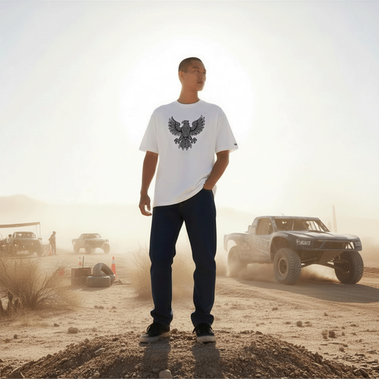 Model wearing Studio Viekay Eagle Engraved Art Box Tee standing in a desert setting with off road vehicles in the background