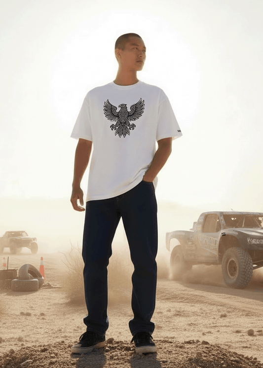 Model wearing Studio Viekay Eagle Engraved Art Box Tee standing in a desert setting with off road vehicles in the background