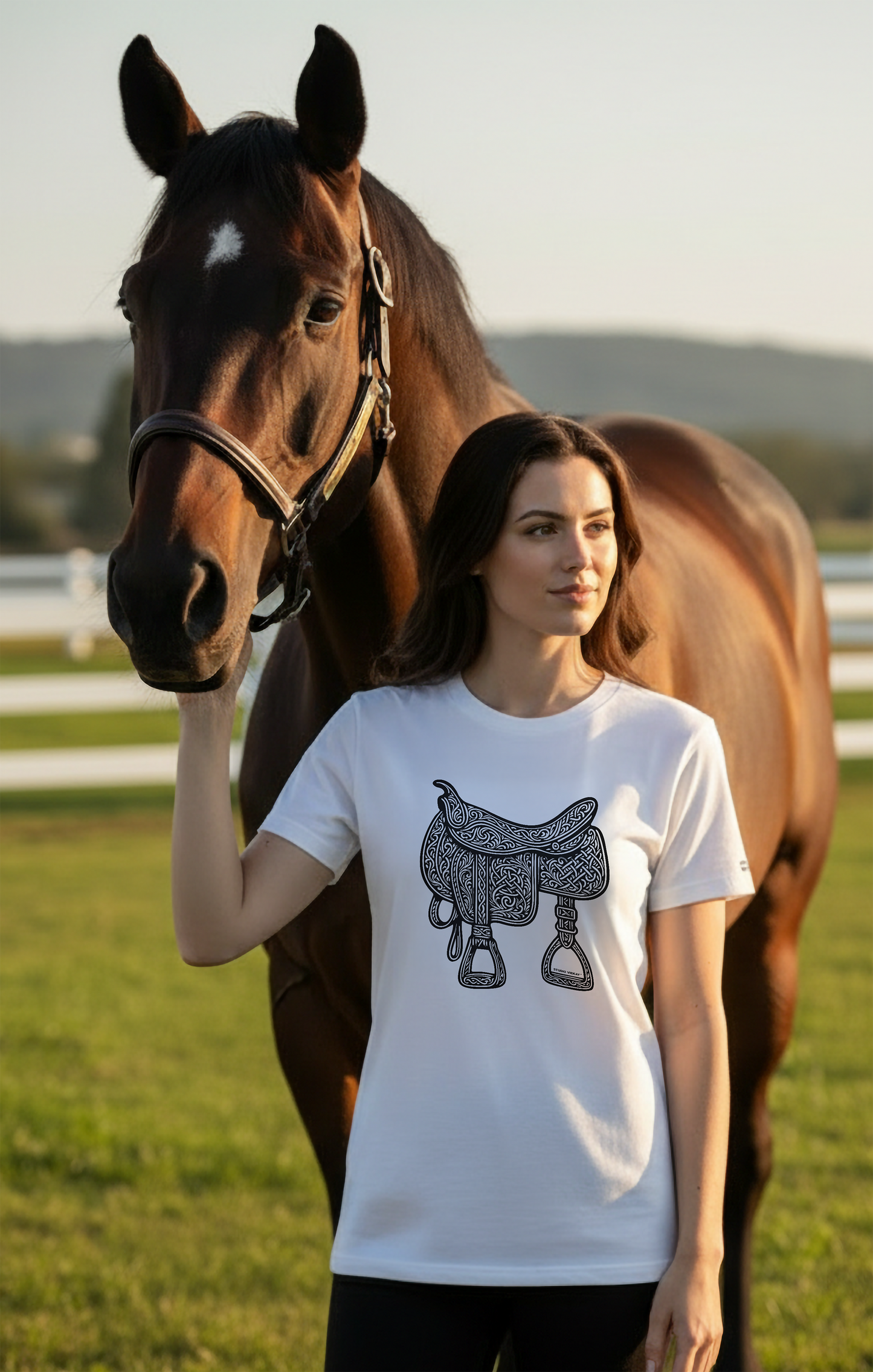 Model wearing a white Studio VieKay t-shirt with a horse saddle graphic, standing next to a horse in an outdoor setting.