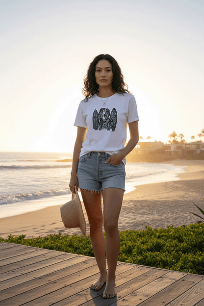 Model standing on a wooden deck by the beach at sunset, wearing a graphic tee by Studio Viekay and denim shorts.